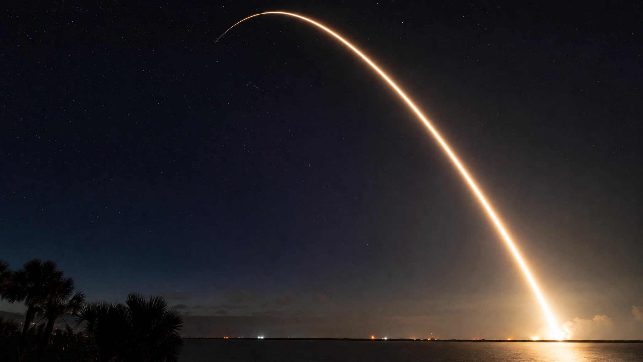 Long-exposure photo of a Falcon 9 rocket trail arcing into the night sky during a Starlink mission launch